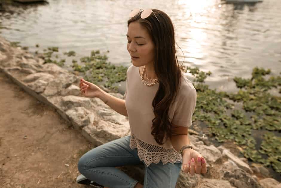 A person meditating peacefully by a serene lake at sunset, surrounded by nature. - Holistic Drug Rehab